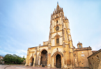 Fototapeta premium Close-up view of the Gothic-style Cathedral of San Salvador in Oviedo, Spain, highlighting its ornate tower and intricate architectural details under a bright blue sky in the historic city center.