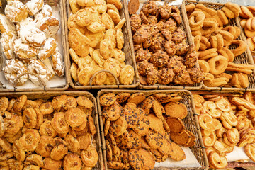 A vibrant assortment of cookies and pastries arranged in wicker baskets, featuring various textures, toppings, and shapes. The display includes iced pastries, nut-topped cookies, chocolate chip treats