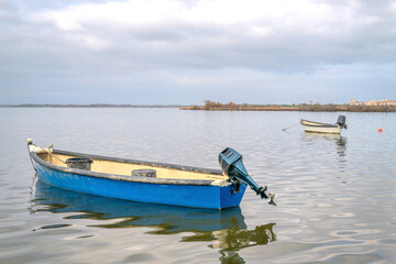 Obraz premium Small traditional fishing boats anchored in the calm lagoon waters of Canet-en-Roussillon, a coastal village in southern France, with overcast skies and soft reflections creating a tranquil atmosphere