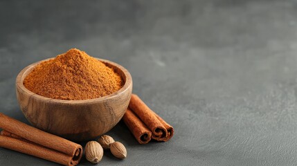 A wooden bowl of ground spice with cinnamon sticks and nutmegs on a gray surface.
