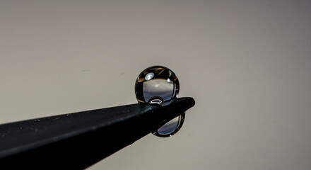 Captivating Water Drop Suspended On Dark Tweezer Point In Delicate Balance