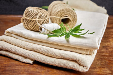Close-up image of a green leaf, ball, skein, spool of natural hemp fiber thread on hemp fabric,...