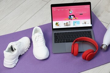 Laptop with sport blog web site and different gym stuff on floor, above view