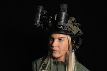 Young blonde woman in a military helmet with night vision goggles, looking to the side, studio shot on a black background.