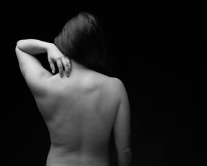 Black and white nude brunette woman seen from behind with one hand on shoulders