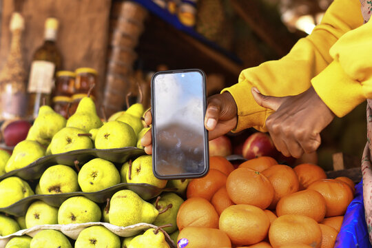 Person holding a smartphone in front of a fruit stand.