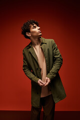 Handsome young man in stylish green coat poses against vibrant red backdrop