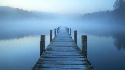 Fototapeta premium Misty morning view of a wooden pier extending into a calm lake shrouded in fog.