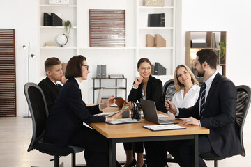 Coworkers with different devices working together at wooden table in office
