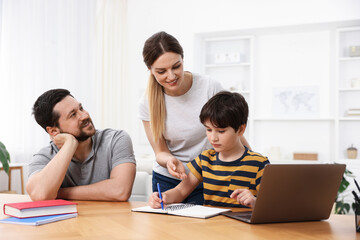 Parents helping their son with homework at wooden table indoors