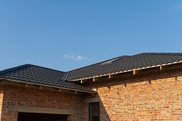 A newly finished brick house features a sleek black tiled roof under a clear sunset sky with scattered clouds, highlighting modern architecture