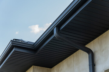 Close view of a roof edge and downspout against a bright blue sky highlights contemporary...
