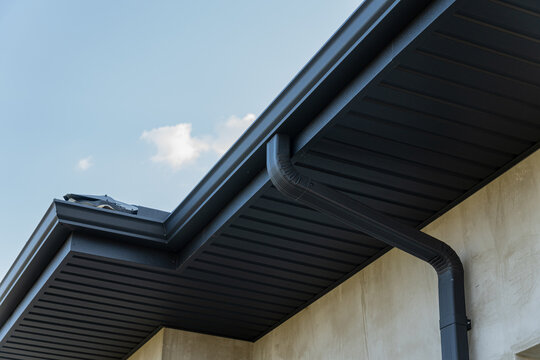 Close view of a roof edge and downspout against a bright blue sky highlights contemporary construction features and materials