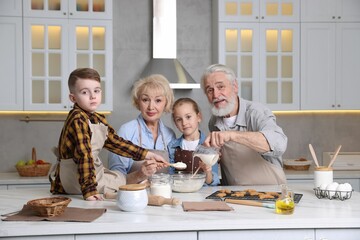 Grandparents and their grandkids cooking together at white marble table in kitchen