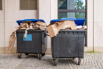&Uuml;berf&uuml;llte Altpapier-Tonnen mit Kartonabf&auml;llen vor einem B&uuml;rogeb&auml;ude