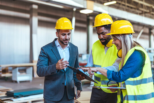 Engineers Collaborating in a Factory Setting With Safety Helmets and High-Visibility Vests