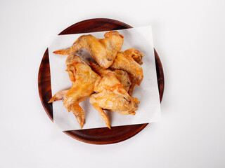 Fried chicken wings on paper towels on a wooden plate with a white background