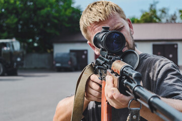 The soldier aims at his weapon. Standing, aiming his assault rifle. Close-up portrait.