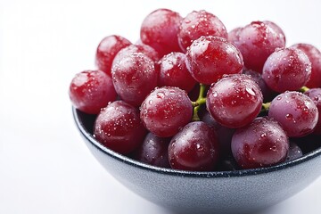 A bowl of vibrant red grapes, with water droplets on their smooth skin, placed on a clean white backdrop