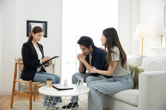 Stressed Asian man holding hands in worry while partner comforts beside, emotional tension from workplace failure, couple facing life challenge and considering professional mental health counseling