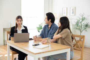 Asian couple sitting at table discussing property options with female real estate agent, showing trust, planning, and communication during home buying decision in relaxed lifestyle environment