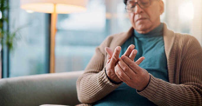 Hands, home and old man with pain, muscle tension or inflammation with arthritis in living room. Fibromyalgia, pensioner or elderly person on sofa, osteoporosis or parkinson disease with injury