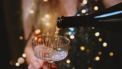 Women's hands hold round glasses, pour champagne. Women in a sparkling dress