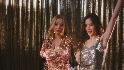 The girl opens a bottle of champagne. A woman in a sparkling dress uncorks a bottle of alcohol