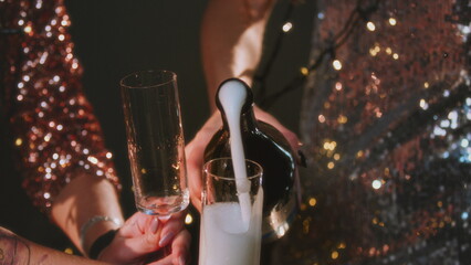 The girl opens a bottle of champagne. A woman in a sparkling dress uncorks a bottle of alcohol