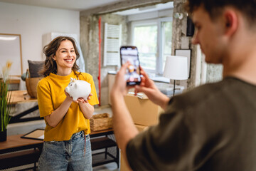 man use mobile phone for shooting woman with piggy bank around boxes