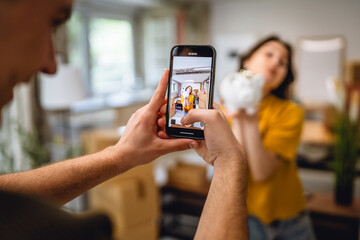 man use mobile phone for shooting woman with piggy bank around boxes