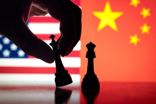 Hand tipping king piece in front of USA and China flags, representing strategic rivalry, trade war, and growing global competition between the United States and China