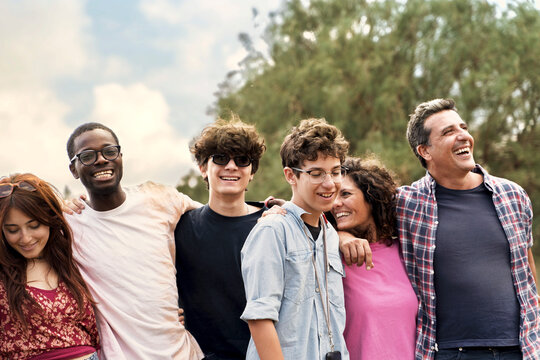 Happy diverse group of friends with arms around each other, laughing outdoors in a multicultural portrait