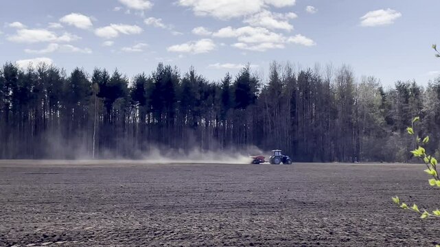 4k motion blue tractor with seeder in plowed field near pine forest on sunny spring day