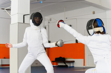Female fencer lunging forward to strike opponent indoors.