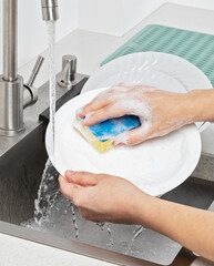 Housewife washing white plate with sponge in kitchen sink