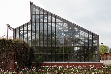 Obraz premium Glass greenhouse building with sharp corners and flowers in the foreground.