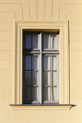 Classic window with reflections on beige wall. Vintage architecture with decorative frame. Old building facade detail. Historical element with light. Exterior structure in urban city background.