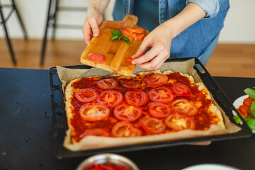 Cooking homemade pizza. Female hands making dough, adding sauce and ingredients.