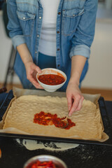 Cooking homemade pizza. Female hands making dough, adding sauce and ingredients.