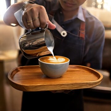 Barista sirviendo capuchino con latte art en una bandeja de madera