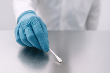 Precision Sample Analysis: A gloved hand delicately holds a sterile cotton swab over a shiny, metallic surface, ready for meticulous examination in a controlled laboratory environment.