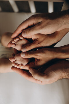 The central element of the image is the baby's legs, which are gently embraced by a man's and a woman's palms. A symbol of warmth, care, and family. 