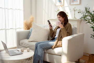 Young Woman Enjoying Smartphone While Relaxing in Cozy Living Room Filled With Plants and Sunlight