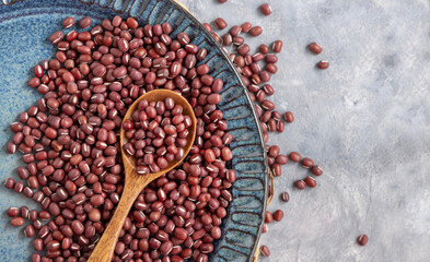 Blue plate full of dried red azuki beans with a wooden spoon top view. Vegetarian protein source
