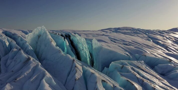 Aerial view of deep crevasses in a glacier under golden sunlight, drone video of icy terrain