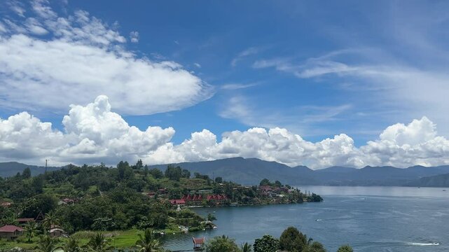 Footage of Danau Toba in North Sumatra, Indonesia, showing calm lake waters and a scenic mountain backdrop under cloudy skies. Captured from an elevated viewpoint in TukTuk, Samosir Island.