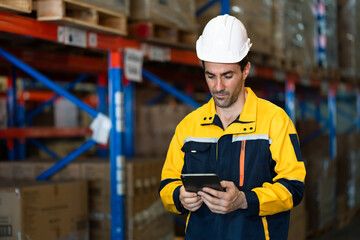 Warehouse employee in yellow protective workwear holding digital tablet checking orders among...
