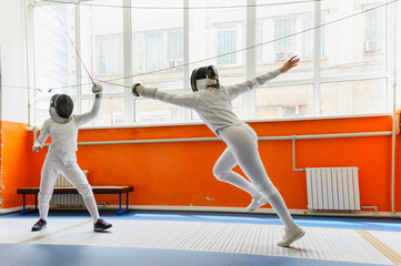 Female fencer making airborne epee attack in bright fencing hall.