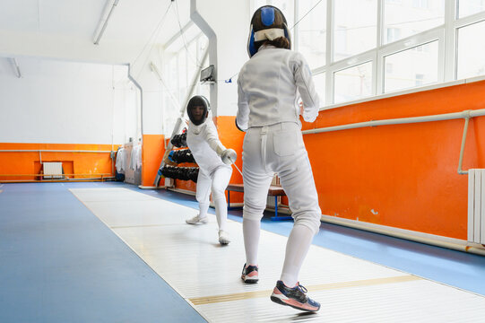 Female fencer lunging toward opponent in bright fencing hall.